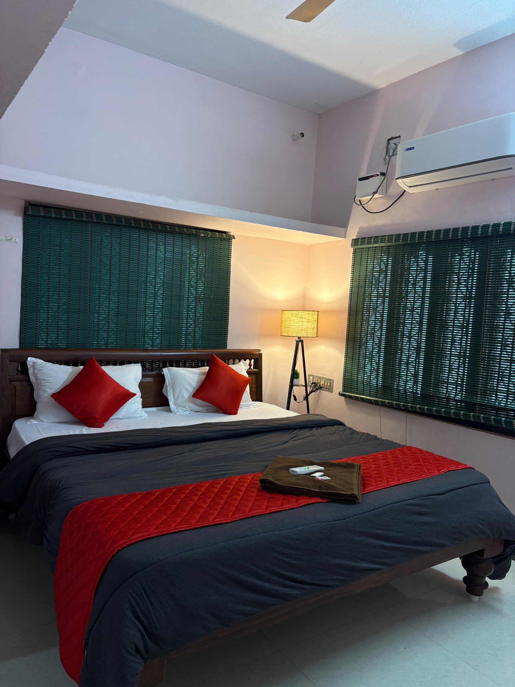 Bedroom with a wooden double bed, red cushions, green window blinds and a split air conditioner