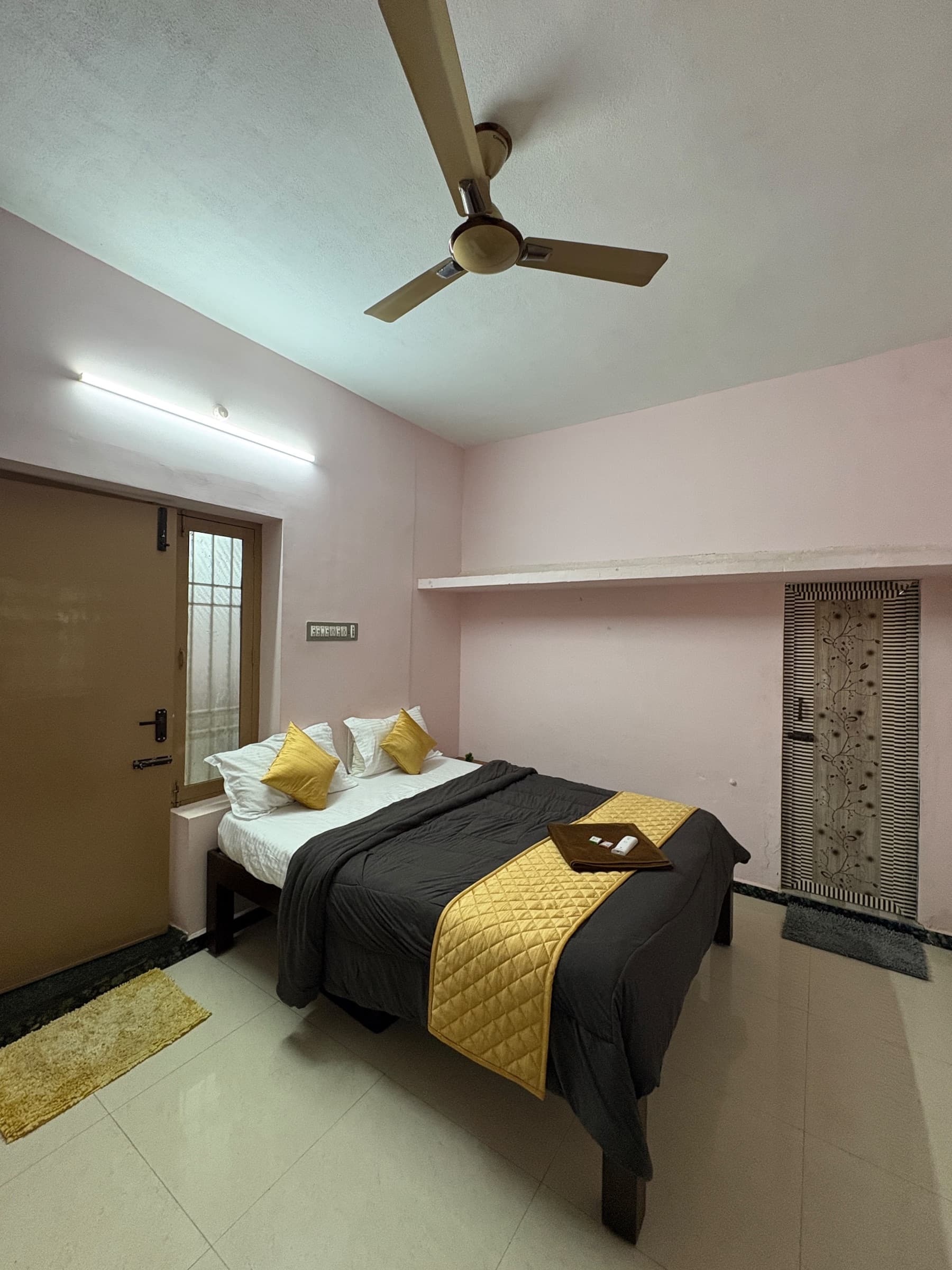 Wide view of the mustard-accented bedroom with a ceiling fan and a patterned door