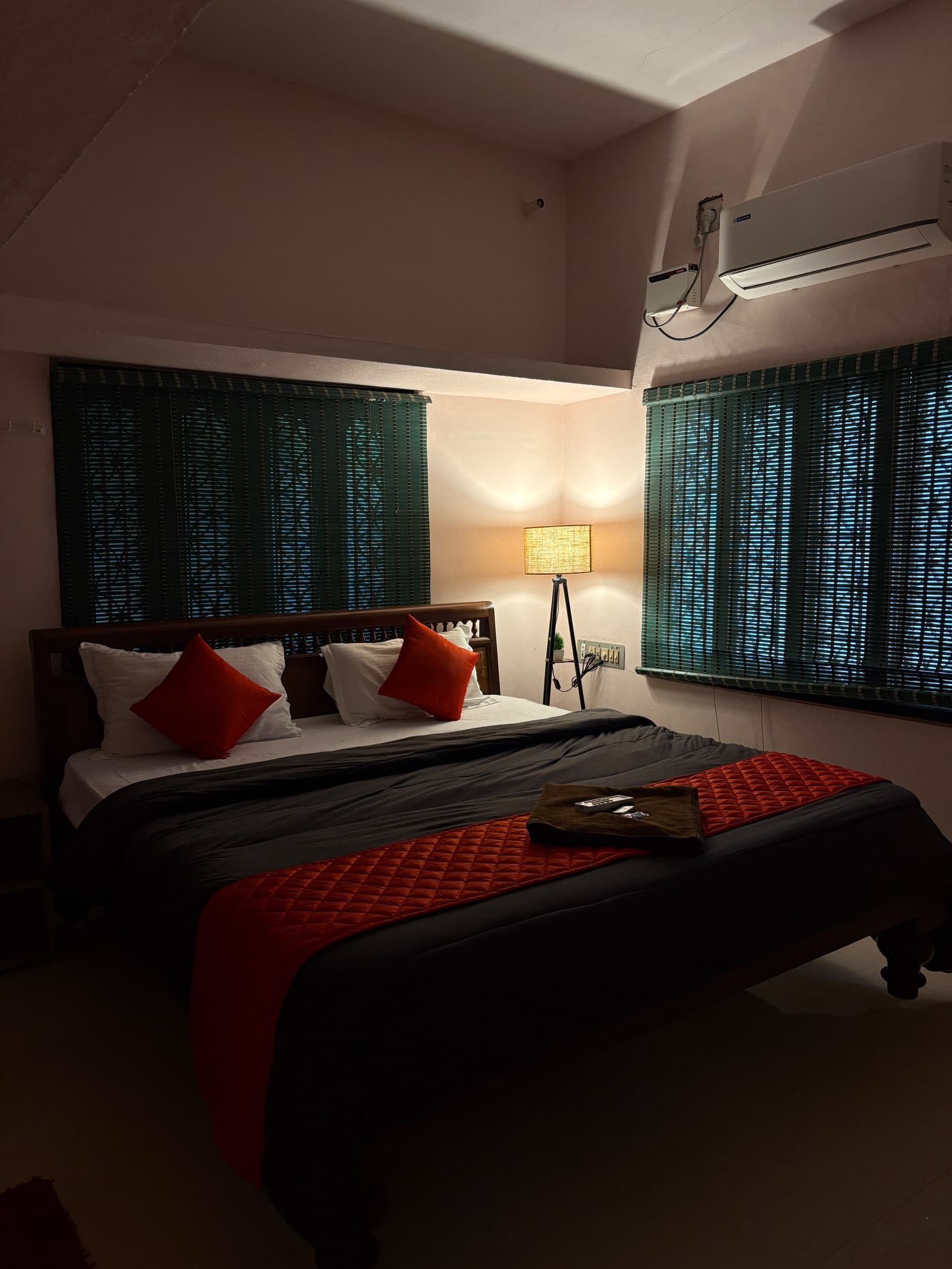 Red-accented bedroom in warm lamplight, with green blinds and air conditioning